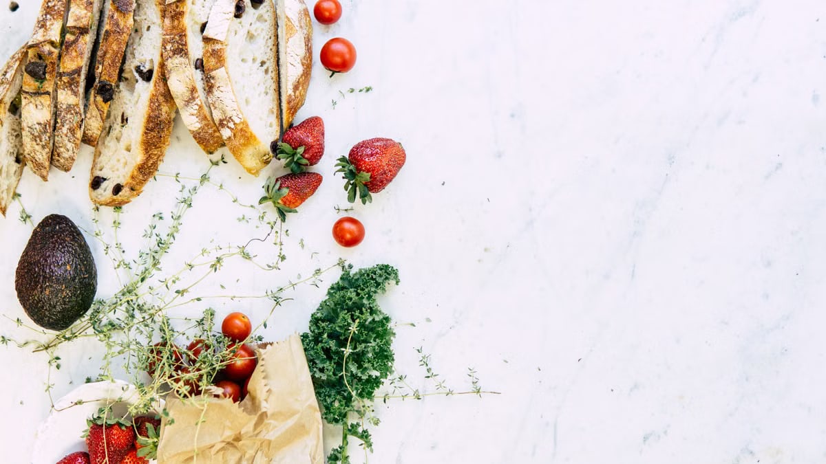 A flat lay of fresh ingredients including bread, strawberries, and avocado on marble. Perfect for food and lifestyle imagery.